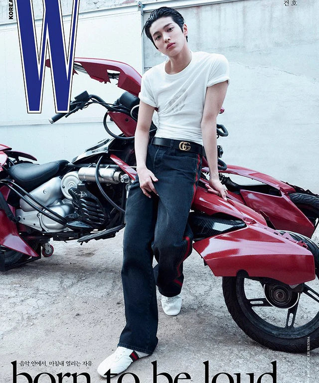 CORTIS's KEONHO posing with a red motorcycle, wearing a white t-shirt and black pants, in front of a magazine cover with 'W' logo.