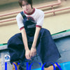 TWS's Kyungmin wearing a white shirt with red accents and blue overalls sitting on a blue surface with 'D-ICONS' branding.