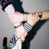 Three people - B1A4 members -  holding hands with visible jewelry against a gray background