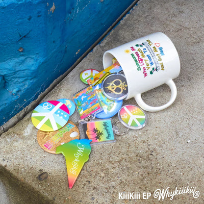 KiiiKiii's EP promo image showing a white ceramic mug tipped over on a concrete surface next to a blue wall, spilling a group of colorful peace-sign themed accessories including round pins, a shield-shaped tag, and acrylic keychains. 