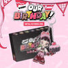 A metal keyring charm featuring a cartoon girl in a pink birthday dress holding a cupcake, shown in front of a black box with the text 'OUR BIRTHDAY! METAL KEYRING VER.' on a pink decorated background.