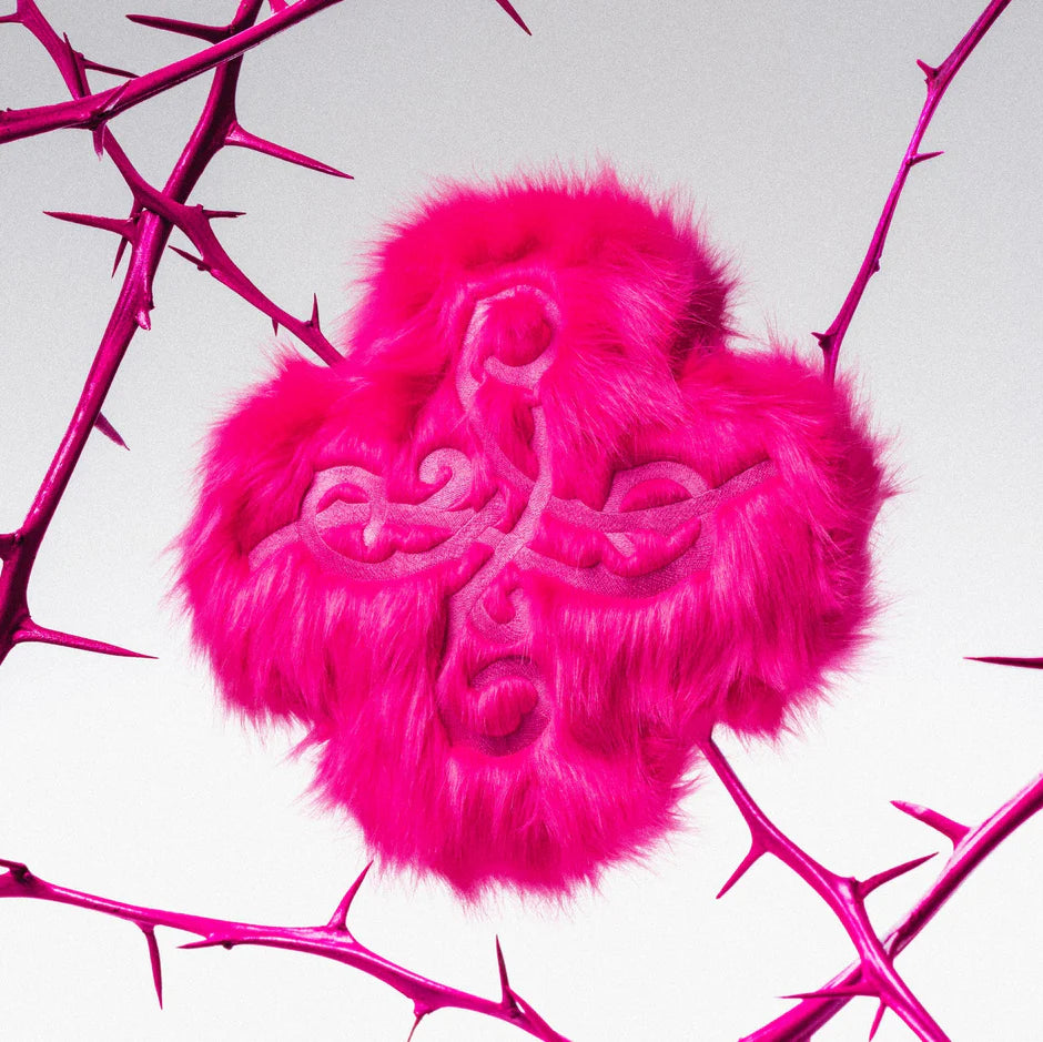 Pink furry heart-shaped object with intricate designs on a pink thorny branch background